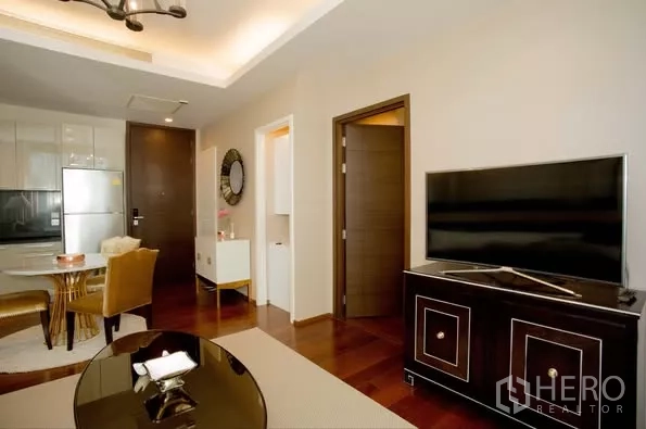 Condominium for rent in Watthana, Bangkok - Living area with TV console, recessed lighting, wooden floors, and doors to bedroom and entry.
