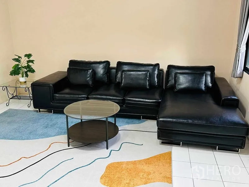 Home Office for rent - Black leather L-shaped sofa with round coffee table on decorative rug.