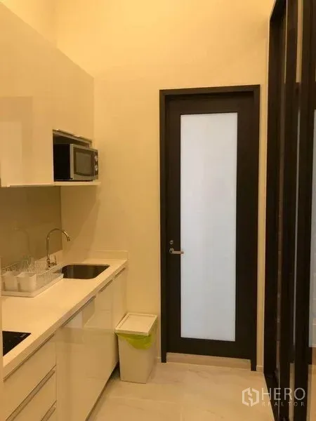 Condominium for sale in Ratchathewi, Bangkok - Galley kitchen with induction hob, microwave and a frosted glass door.