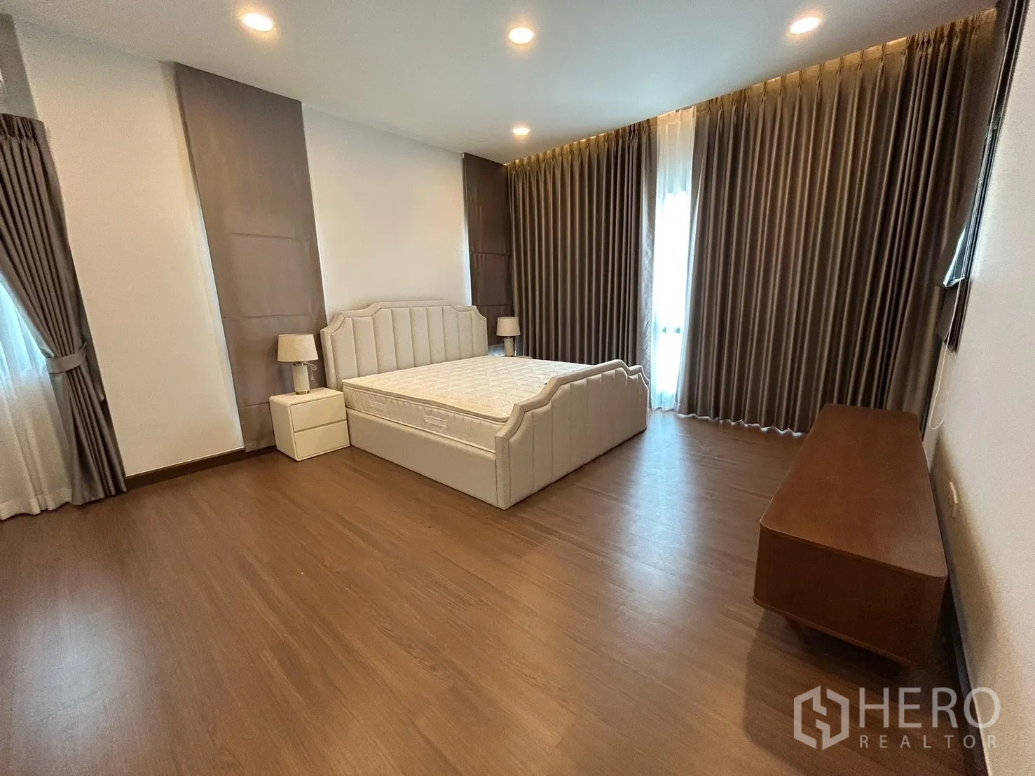 独栋房屋 for rent in Bang Phli, Samut Prakan - 宽敞卧室，软包床、床头柜、木地板与落地窗帘。