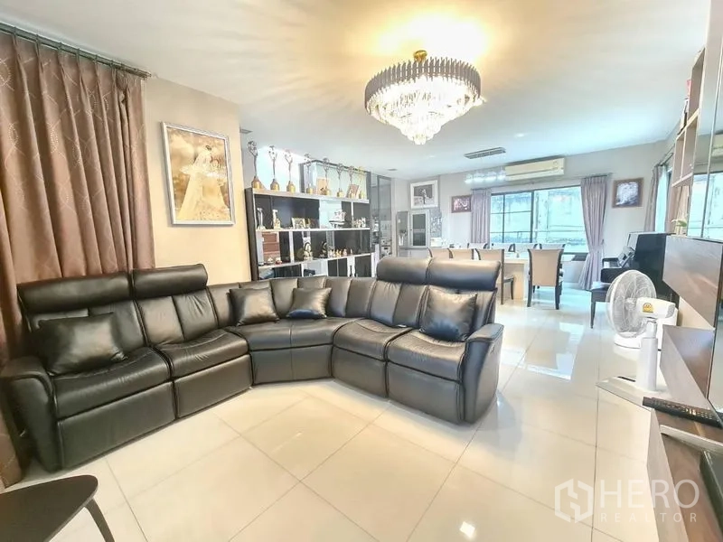 Detached House for sale in Prawet, Bangkok - Spacious living room with black leather sectional sofa, chandelier and glossy tile floor.