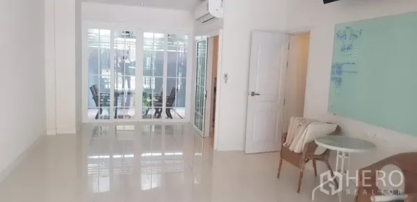 联排别墅 出租在Bang Na, Bangkok - 明亮客厅，亮面地砖，玻璃隔断通向露台，配壁挂空调。