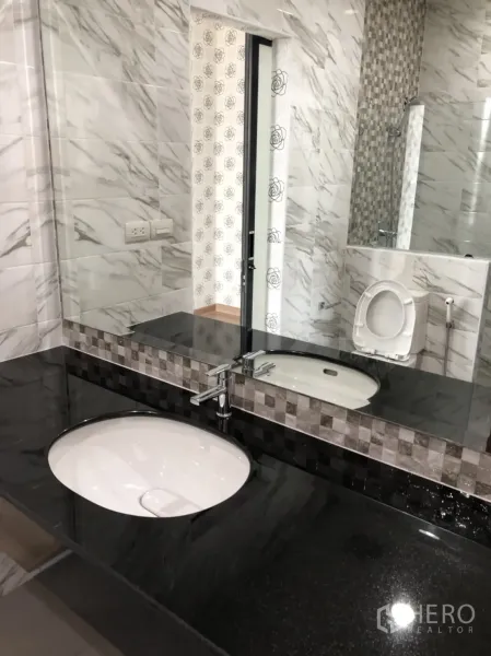 Townhouse for rent in Din Daeng, Bangkok - Modern bathroom with black granite vanity, large mirror, and marble-effect wall tiles.