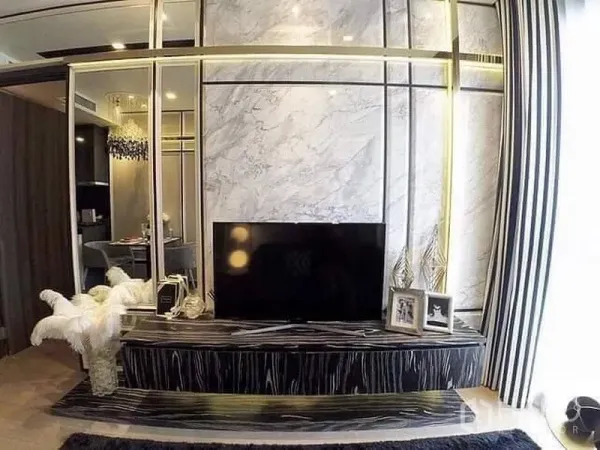 Condominium for rent or sale in Watthana, Bangkok - Modern condo living room with marble feature wall, gold trim, and a black TV console beside striped curtains.