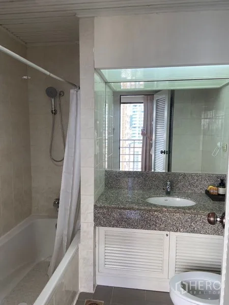 Condominium for rent in Pathum Wan, Bangkok - Bathroom vanity with large mirror and bathtub reflection.