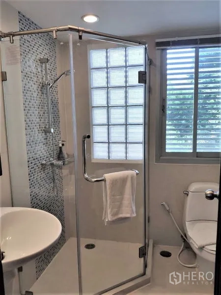 Condominium for rent in Bang Rak, Bangkok - Modern bathroom featuring a glass shower enclosure, mosaic wall and window.