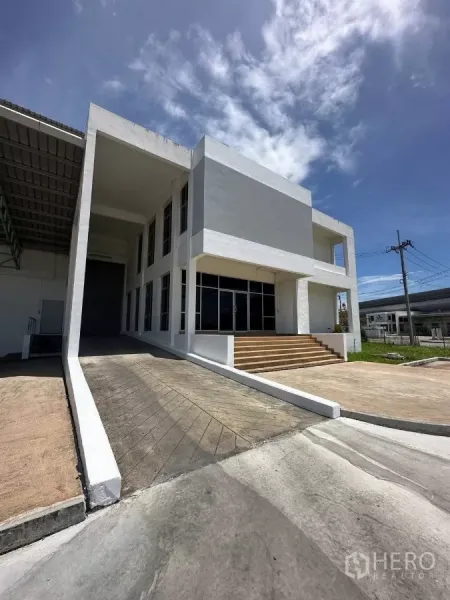 工厂 出租在Si Racha, Chon Buri - 两层现代办公楼，带坡道与台阶，位于厂房一侧，晴空下。