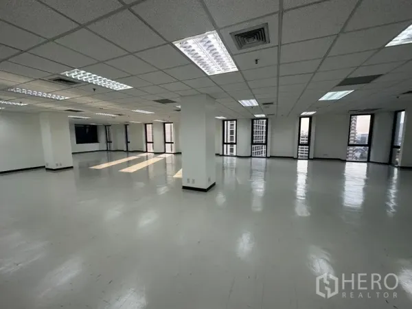 Office Space for rent - Open workspace with tall windows, suspended ceiling, and daylight streaming across the floor.