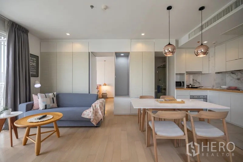 Condominium for rent in Watthana, Bangkok - Living room with floating wall shelves, mounted TV and sliding glass doors to a small balcony.