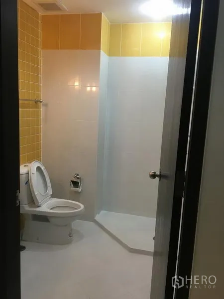Condominium for rent in Khlong Toei, Bangkok - Bathroom with yellow tiles, toilet and a glass-partitioned walk-in shower.