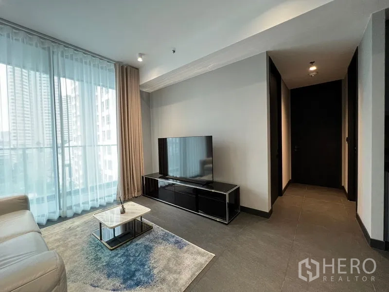 Condominium for rent in Bang Rak, Bangkok - Living room with large TV console, sheer curtains and city-facing windows.