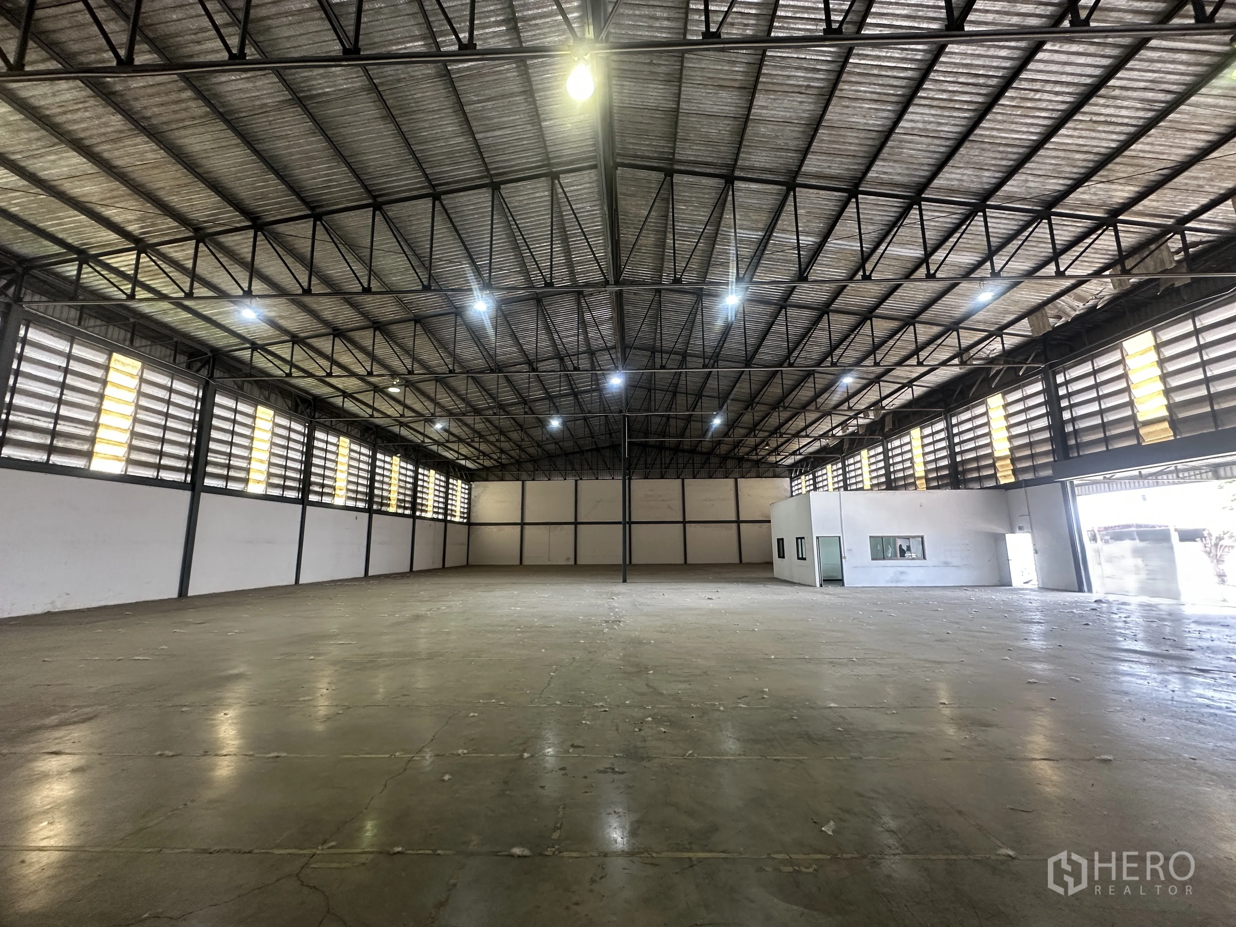 仓库 for rent in Khlong Luang, Pathum Thani - 明亮灯光下的大面积混凝土地面，侧墙百叶窗与一侧办公区。
