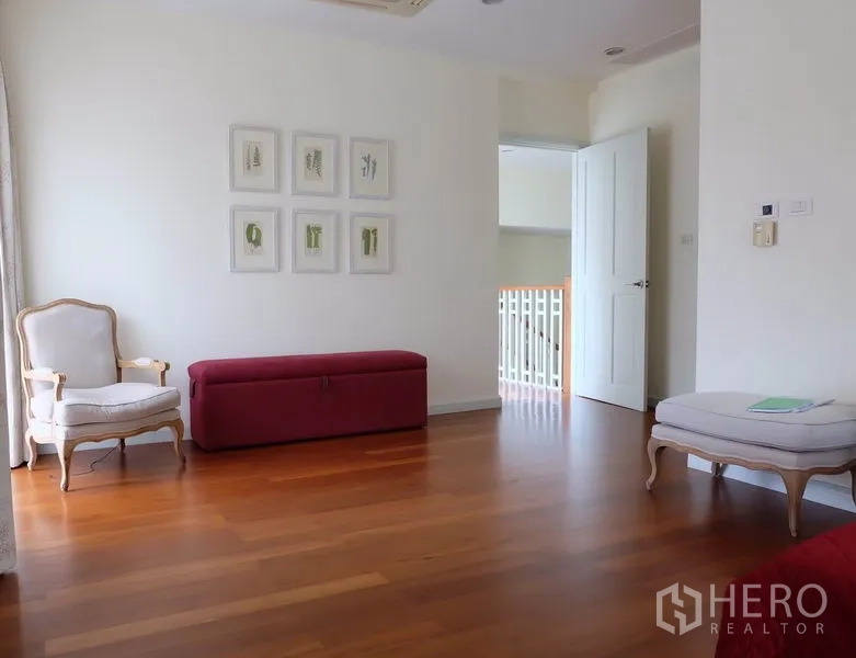 Detached House for rent in Watthana, Bangkok - Upper landing sitting area with classic armchairs, an ottoman bench, and framed wall art.