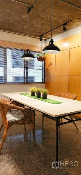 公寓 出售在Watthana, Bangkok - 公寓餐区，长桌与藤椅，工业风吊灯，窗边木饰面墙。