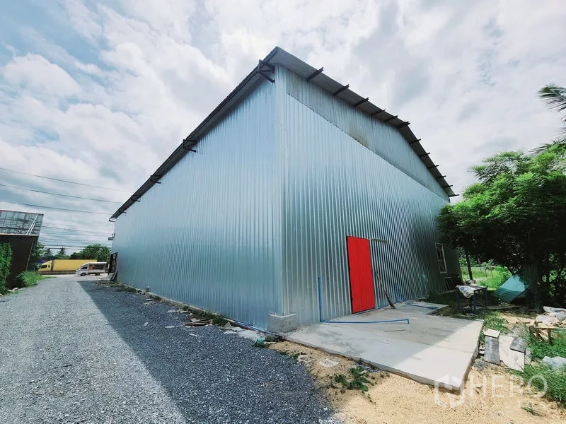 货栈 出租在Sam Phran, Nakhon Pathom - 金属波纹板仓库侧立面，配亮红色侧门与服务通道。