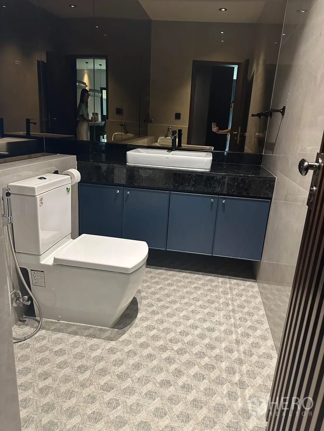 บ้าน ให้เช่าในLat Krabang, Bangkok - ห้องน้ำร่วมสมัย มีกระจกบานใหญ่ ตู้ล่างสีน้ำเงิน และโถสุขภัณฑ์บนพื้นลายกราฟิก