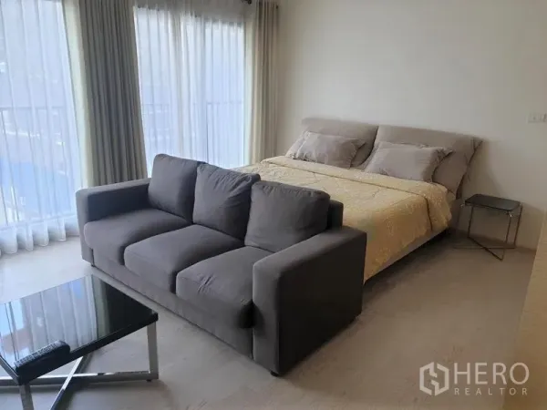 公寓 出租在Khlong Toei, Bangkok - 明亮的睡眠区，配大床、灰色沙发与转角落地窗