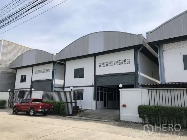 货栈 出租在Pak Kret, Nonthaburi - Pak Kret 现代仓库外观，弧形金属屋顶与卷帘门，带围栏入口