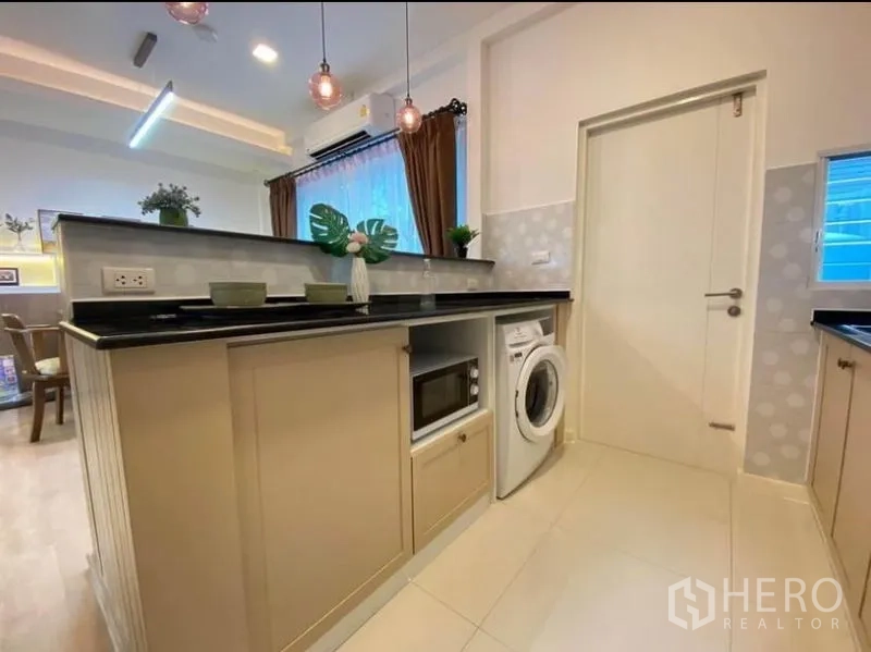 联排别墅 出租在Prawet, Bangkok - 厨房半岛台，黑色台面，内置微波炉与洗衣机，吊灯点缀。