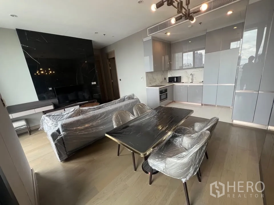 公寓 出租在Huai Khwang, Bangkok - 四人餐桌旁为亮灰色厨柜与大理石防溅板，电视背景墙相对。