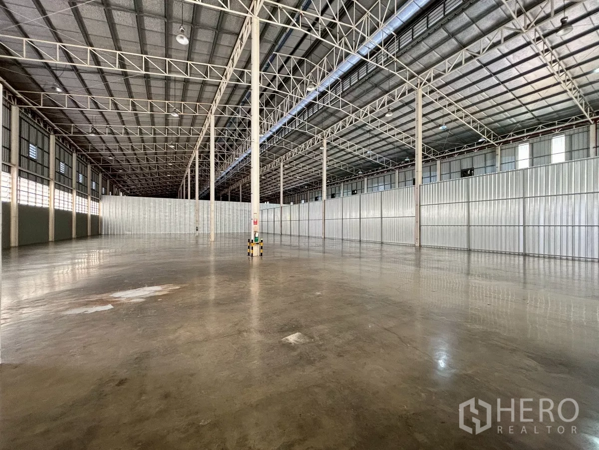 Warehouse for rent in Bang Sue, Bangkok - Empty storage hall with polished concrete slab, louvered windows and fire safety signage on columns.