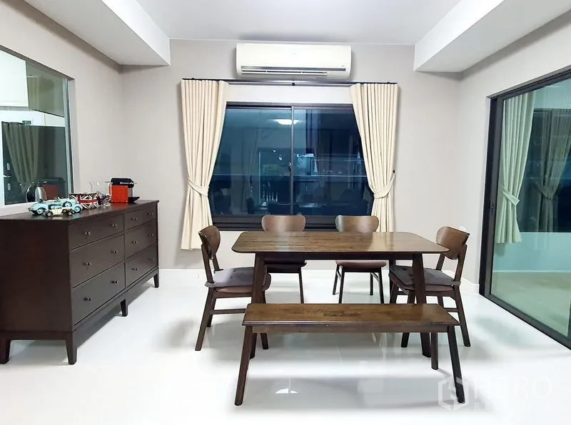 Detached House for rent in Bang Phli, Samut Prakan - Dining area with wooden table and bench seating beside large windows and curtains