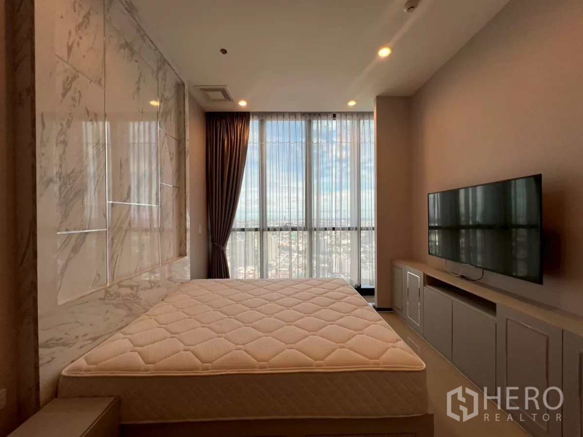 Condominium for rent in Phra Khanong, Bangkok - Primary bedroom with marble feature wall, TV console, and full-height windows facing skyline.
