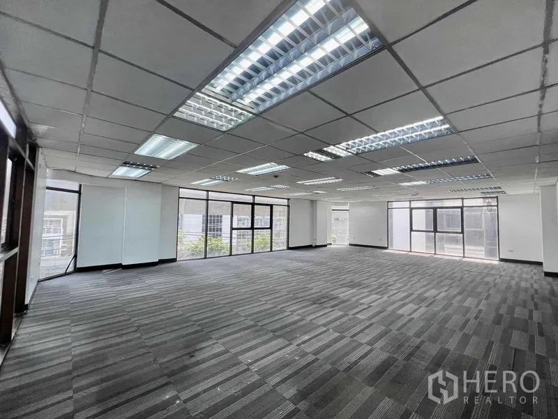 Shophouse for rent in Khlong San, Bangkok - Large open-plan office with carpet tiles, grid ceiling and floor-to-ceiling windows.