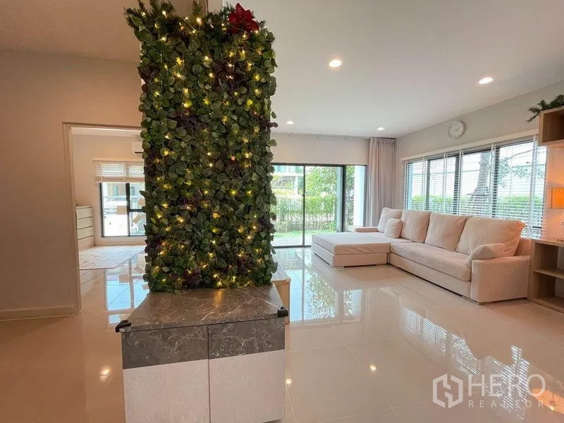 独立式住宅 出售在Pak Kret, Nonthaburi - L形沙发的采光客厅，推拉门通向花园。