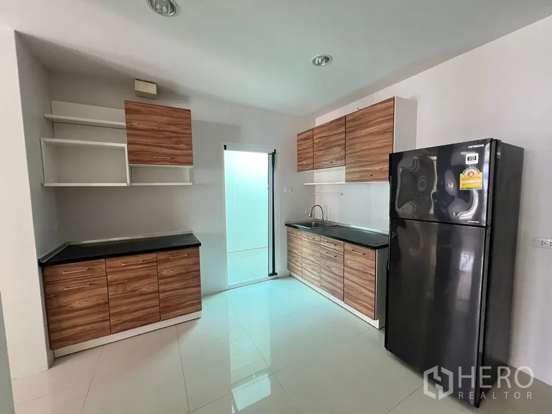 Townhouse for rent in Din Daeng, Bangkok - Compact kitchen with wood-grain cabinetry, black countertops, sink and door to the utility area.