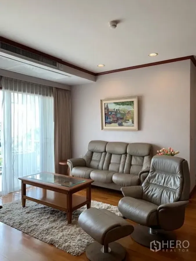 公寓 出租在Khlong Toei, Bangkok - 起居区设沙发、扶手椅与脚凳、地毯和装饰画，连接阳台。