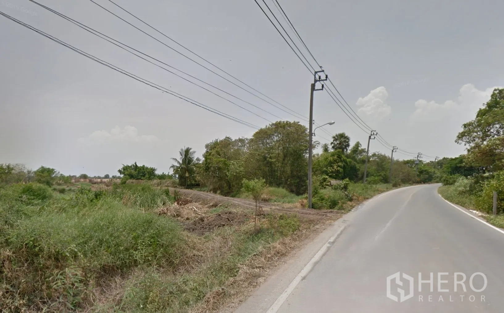 Land for sale in Bang Bo, Samut Prakan - Concrete road curving past open land with trees and power lines in Bang Bo, Samut Prakan.