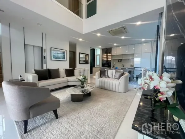 Detached House for rent in Bueng Kum, Bangkok - Open-plan living area with modern sofas, rug and view toward a sleek white kitchen.
