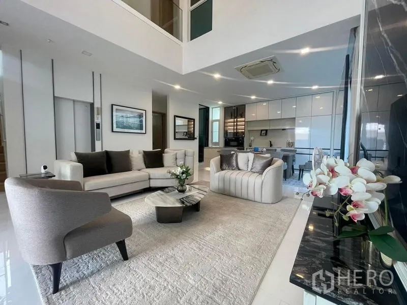 Detached House for rent in Bueng Kum, Bangkok - Open-plan living area with modern sofas, rug and view toward a sleek white kitchen.
