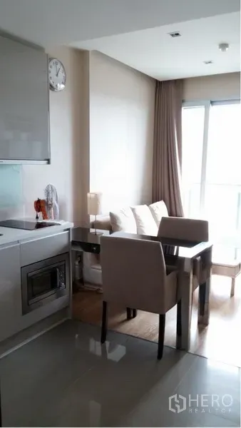 Condominium for rent in Ratchathewi, Bangkok - Open-plan dining and living area beside the kitchenette, filled with natural light from balcony windows.