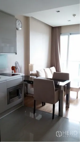 Condominium for rent in Ratchathewi, Bangkok - Open-plan dining and living area beside the kitchenette, filled with natural light from balcony windows.
