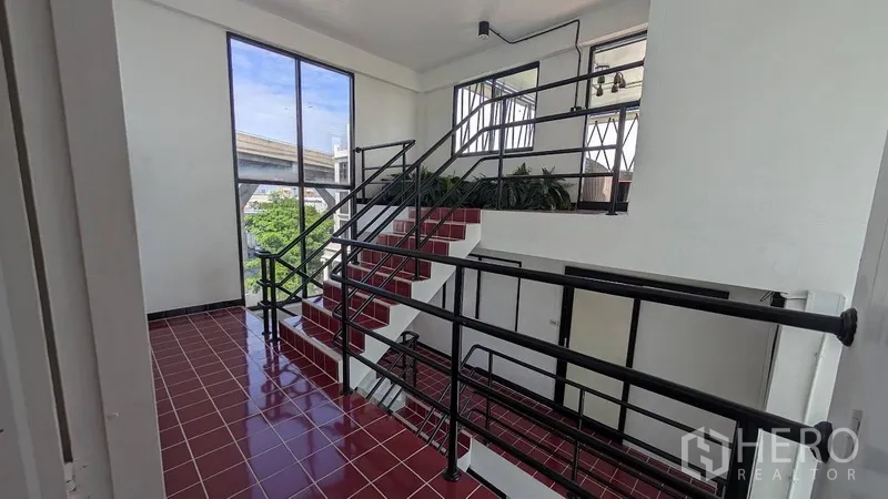 带办公室的家 出租或出售在Phra Khanong, Bangkok - 楼梯平台，红色亮面地砖，大窗与黑色扶手。