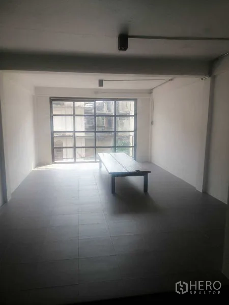 Shophouse for rent in Khlong Toei, Bangkok - Spacious room with window wall and a center bench, ideal for display or seating.