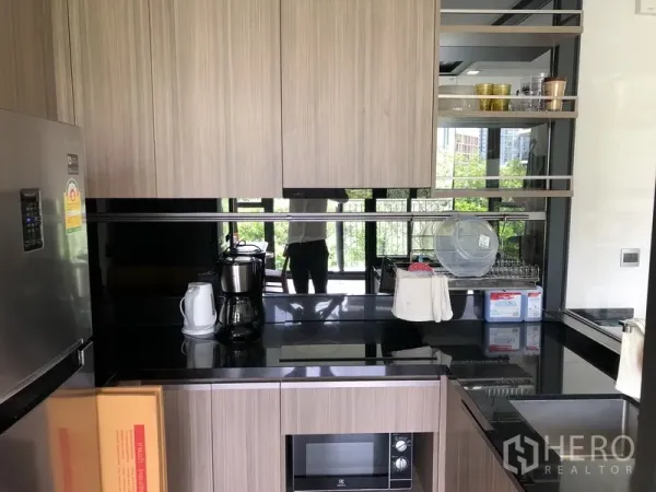 Condominium for rent in Watthana, Bangkok - Compact U-shaped kitchen with wood-grain cabinets, cooktop, microwave, sink, and open shelving.
