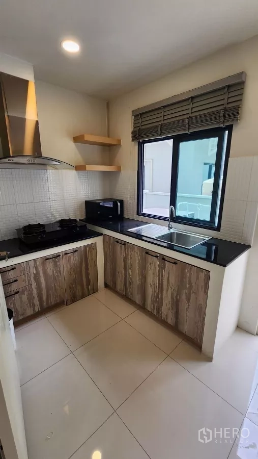 Detached House for rent in Bang Phli, Samut Prakan - L-shaped kitchen with gas hob, range hood, black countertops, sink and window.