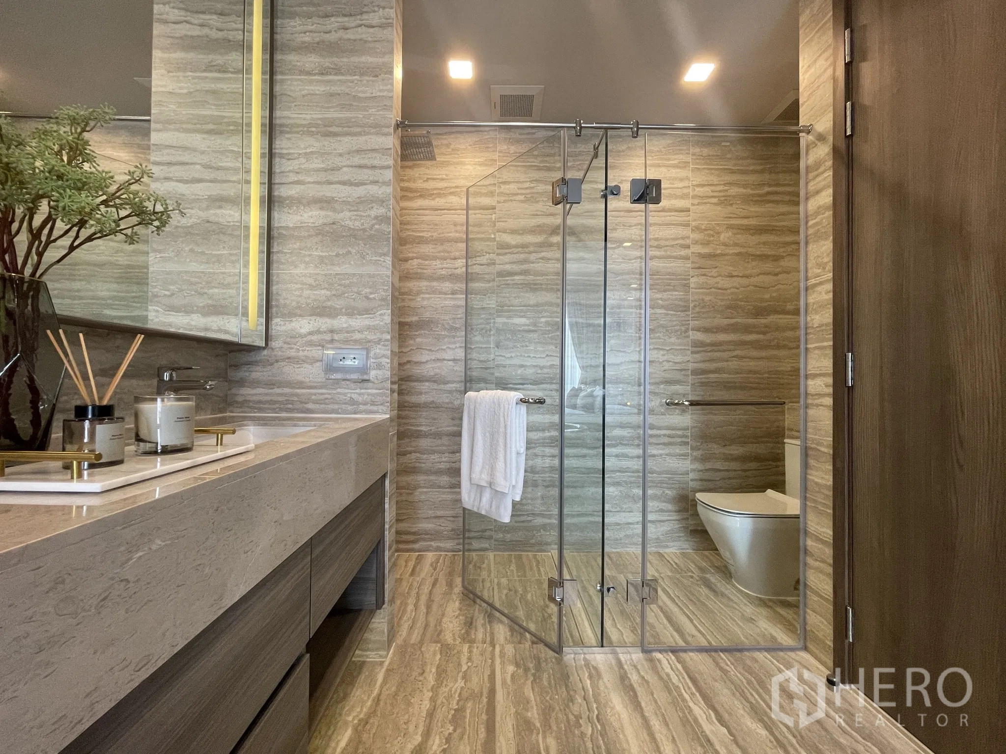 Condominium for rent in Watthana, Bangkok - Bathroom with glass-enclosed shower, stone tiles, and wide countertop.
