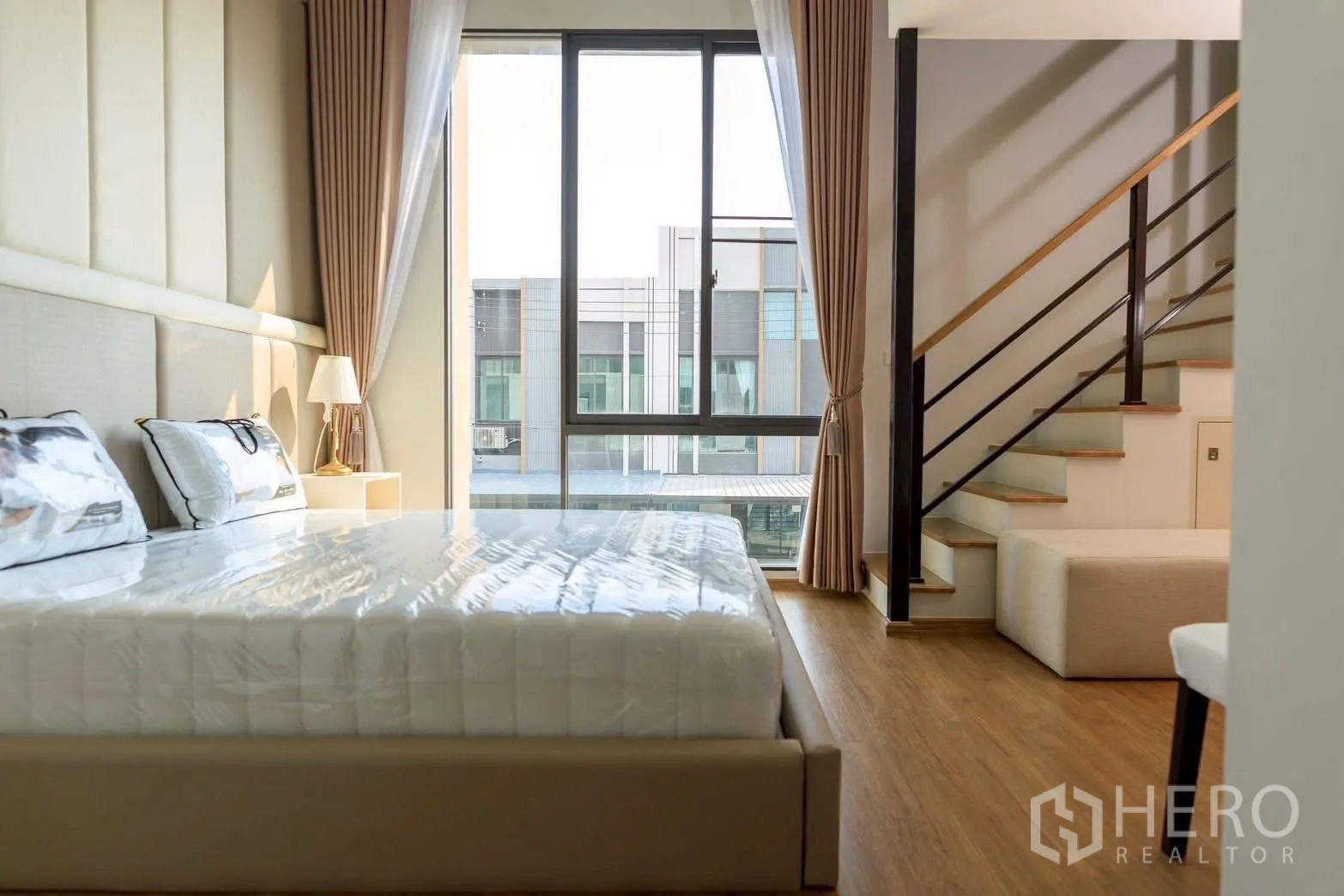 Townhouse for rent or sale in Bang Phli, Samut Prakan - Bedroom with large window, sheer curtains and stairs leading to a mezzanine seating area.