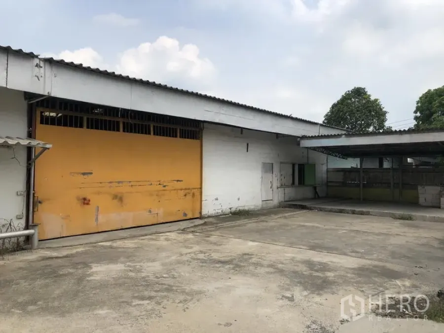 Warehouse for rent in Sai Mai, Bangkok - Private loading court with canopy, white walls, and a wide yellow shutter door.