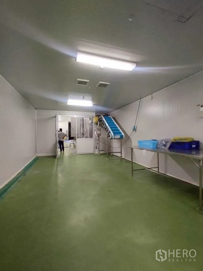 Factory for rent or sale in Mueang Nakhon Pathom, Nakhon Pathom - Clean processing room with green epoxy floor, stainless tables, and a conveyor line under bright lights.
