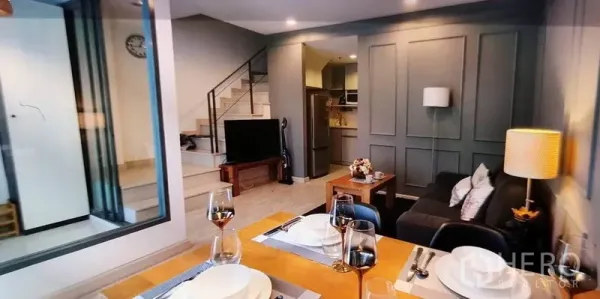 Condominium for rent in Phra Khanong, Bangkok - Living zone with TV console, staircase and kitchenette in view.