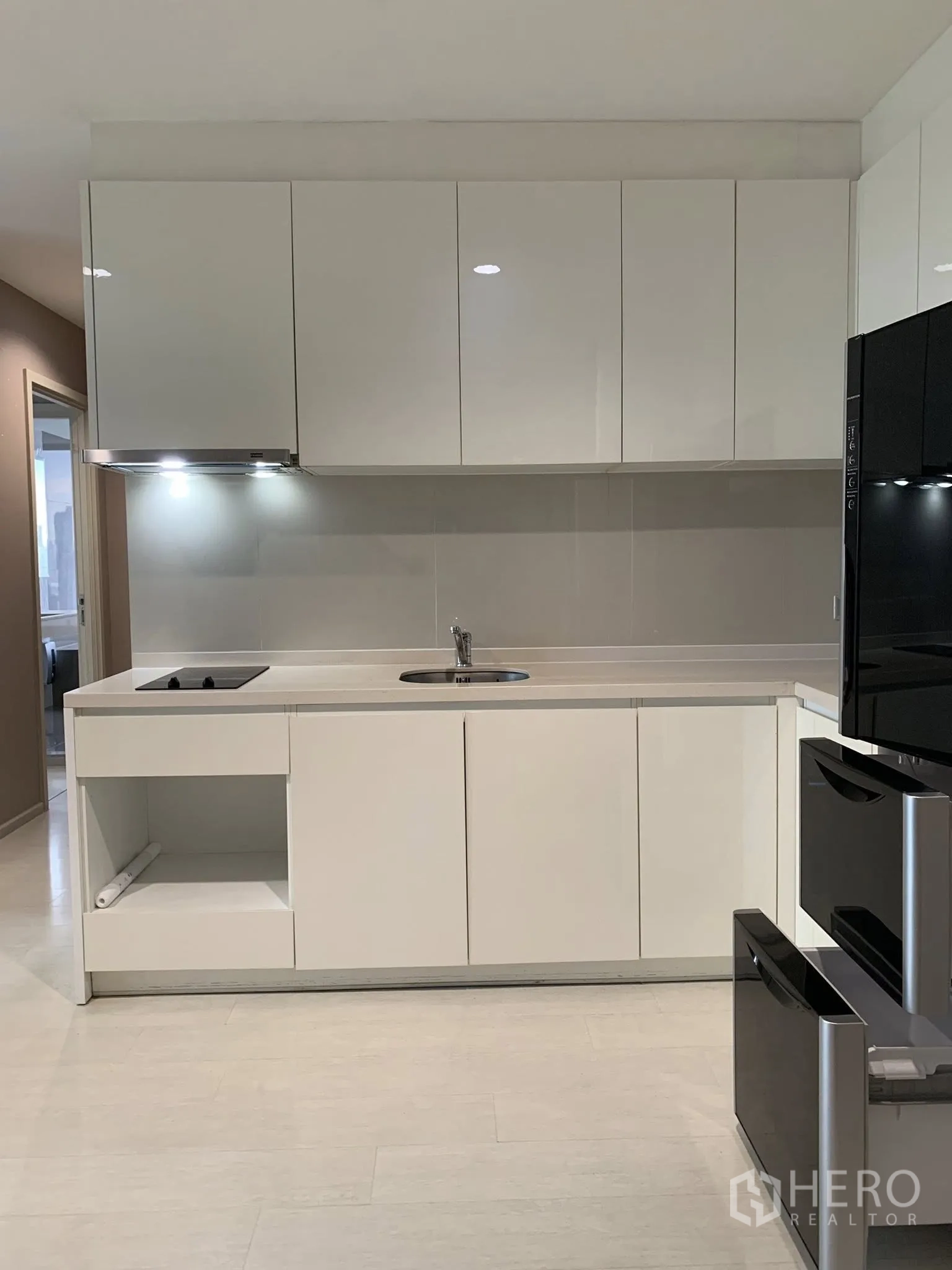 Condominium for rent in Khlong Toei, Bangkok - Sleek white kitchen with upper and lower cabinets, cooktop, hood, and ample counter space.