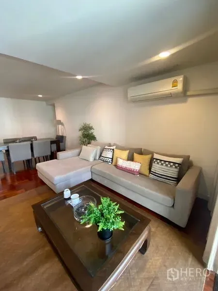 Condominium for rent in Pathum Wan, Bangkok - Bright living room with sectional sofa and air conditioner.