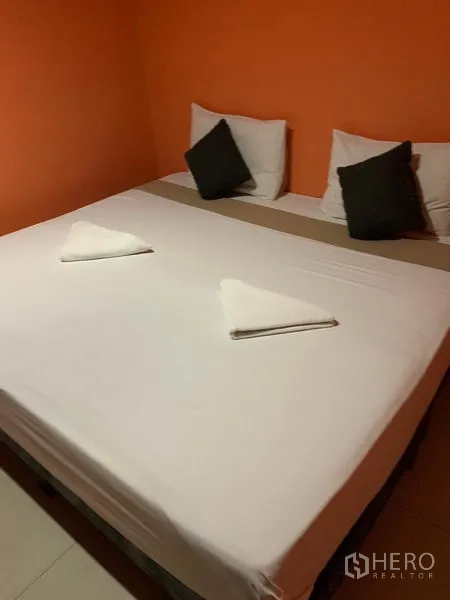 พื้นที่ขายปลีก ให้เช่าในKhlong Toei, Bangkok - เตียงคิงไซส์ในห้องโทนส้ม พร้อมผ้าขนหนูพับวางบนเตียง