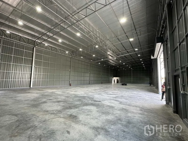 Warehouse for rent in Pak Kret, Nonthaburi - High-clearance warehouse floor with multiple LED lights and metal wall panels.