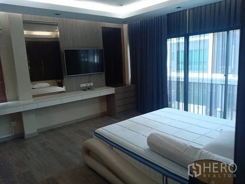 Detached House for rent in Thanyaburi, Pathum Thani - Spacious master bedroom with TV wall, balcony doors, and large windows with layered curtains.